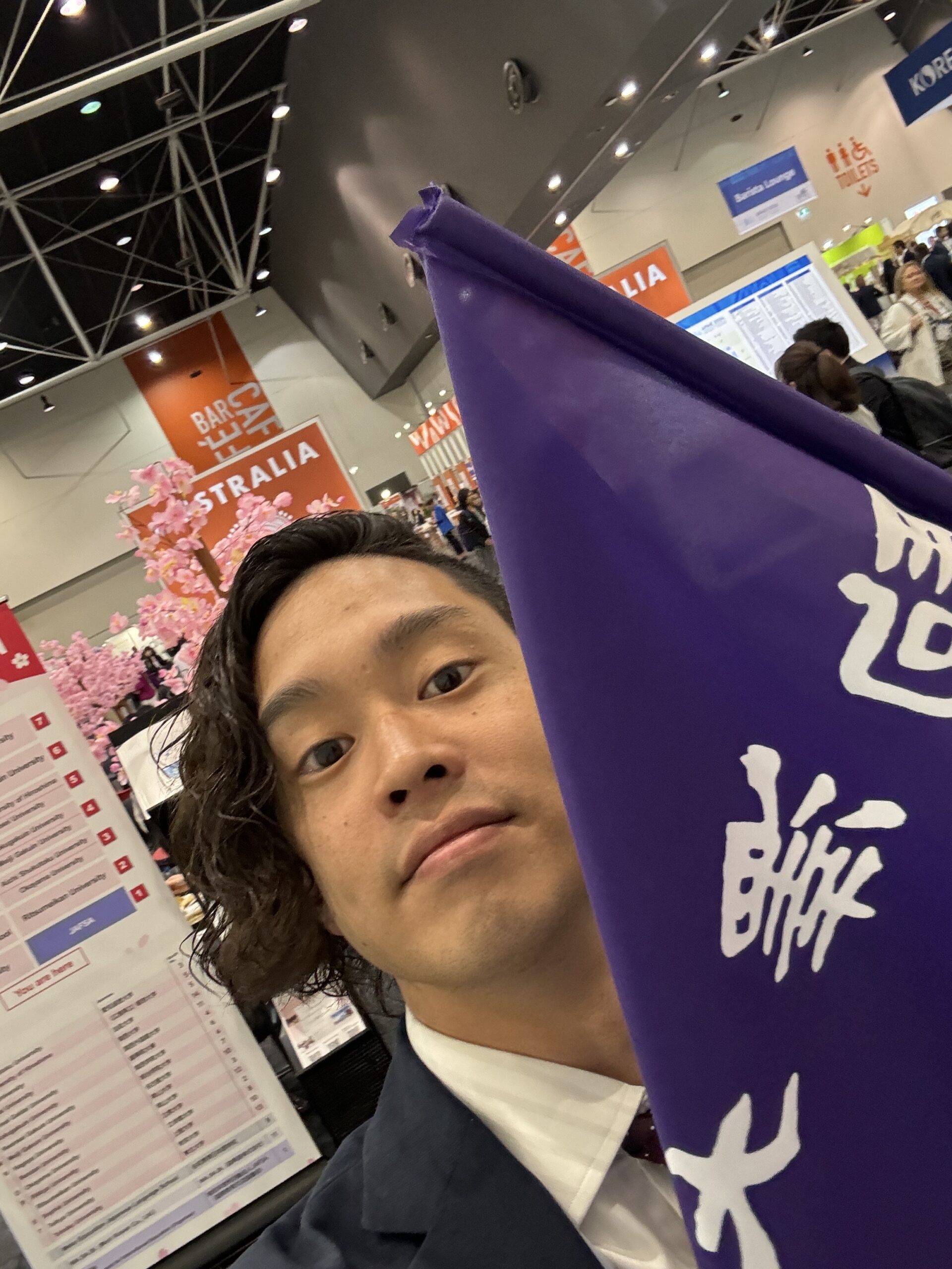 「Study in Japan」ブース付近で大学のフラッグを持ち、ミーティング相手を待つ岡田